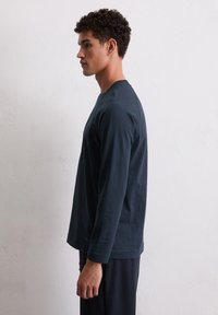 Langarmige marineblauwe shirt van zachte stof, met een ronde hals en een relaxte pasvorm. Zichtbare stiksels bij de mouwen en de zoom. Textuur op het oppervlak.