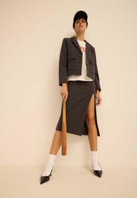 Blazer gris cintré avec deux poches avant, associé à une jupe crayon grise avec une fente sur le côté. Porté avec un t-shirt blanc et des escarpins noirs.