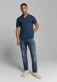 Marineblauw korte mouwen polo shirt gemaakt van zachte stof, gecombineerd met vervaagde blauwe spijkerbroek en lichte sneakers. Eenvoudig ontwerp met een kraag.