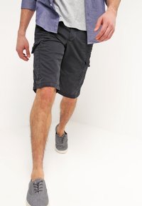 Pantalones cortos de carga de color carbón con bolsillos laterales y un corte relajado, combinados con una camiseta gris y zapatos casuales grises. Textura de tela ligera.