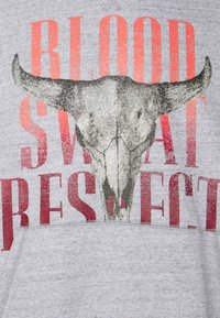 Šedá mikina s metalickým grafikou bílé lebky býka, červeným textem "BLOOD SWEAT RESPECT", s texturovaným povrchem a detaily švů.