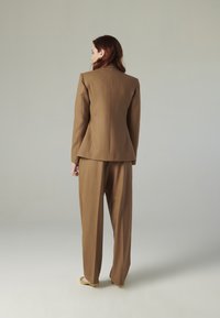 Completo marrone a righe sottili caratterizzato da un blazer su misura con spalline e pantaloni a gamba larga. Tessuto liscio con una silhouette pulita e dettagli minimi.