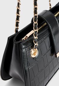 Schwarze handgeprägte Krokolederhandtasche mit goldener Kettenriemen und Reißverschluss, im Nahaufnahme auf neutralem Hintergrund gezeigt.