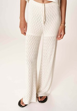 Pantalons en tricot légers de couleur crème avec une coupe ample, dotés d'une taille à cordon de serrage et d'une texture à motifs sur l'ensemble.
