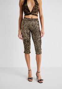 Des pantalons capri en sequins dorés avec une coupe ajustée et un ourlet roulé, associés à un haut halter noir. Des sandales à talons noires avec des nœuds complètent le look.