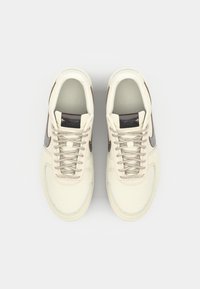 Cremefarvede sneakers med en glat læderoverdel, tekstureret grå Swoosh og lys grå mesh-tunge. Har beige snørebånd og syninger.