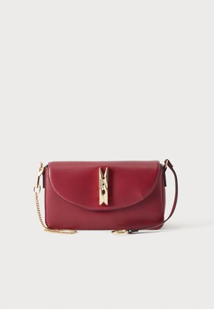 Κόκκινο δερμάτινο τσαντάκι clutch με κούμπωμα σε σχήμα χρυσής μανταλόπετρας, χρυσή αλυσίδα και λουράκι καρπού σε λευκό φόντο.