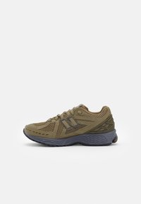 Scarpa sportiva verde oliva con tomaia in rete, dettaglio del logo in rilievo e suola in gomma. Presenta una suola grigia testurizzata per aderenza.