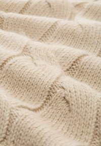 Couverture en tricot beige avec un motif de vagues en relief, mettant en valeur une texture douce et un fil épais, créant une apparence chaleureuse et une sensation tactile.