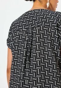 Top in tessuto nero con motivo a zigzag bianco, maniche corte e piega sul retro per una vestibilità comoda.