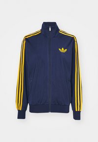 Marinblå zip-up jacka i mjukt tyg, med gula tre-stripes accentuerar på ärmarna och en gul logotyp på bröstet.