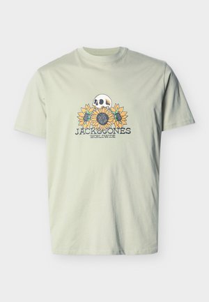 Hellgrünes T-Shirt mit einer Grafik eines Schädels über drei Sonnenblumen und dem Text "JACK & JONES WORLDWIDE" darunter.