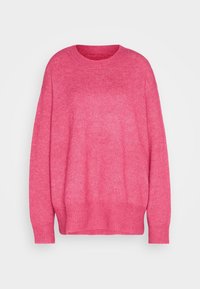 Różowy, miękki, luźny sweter z długimi rękawami oraz ściągaczami przy mankietach, dole i okrągłym dekolcie na neutralnym tle.