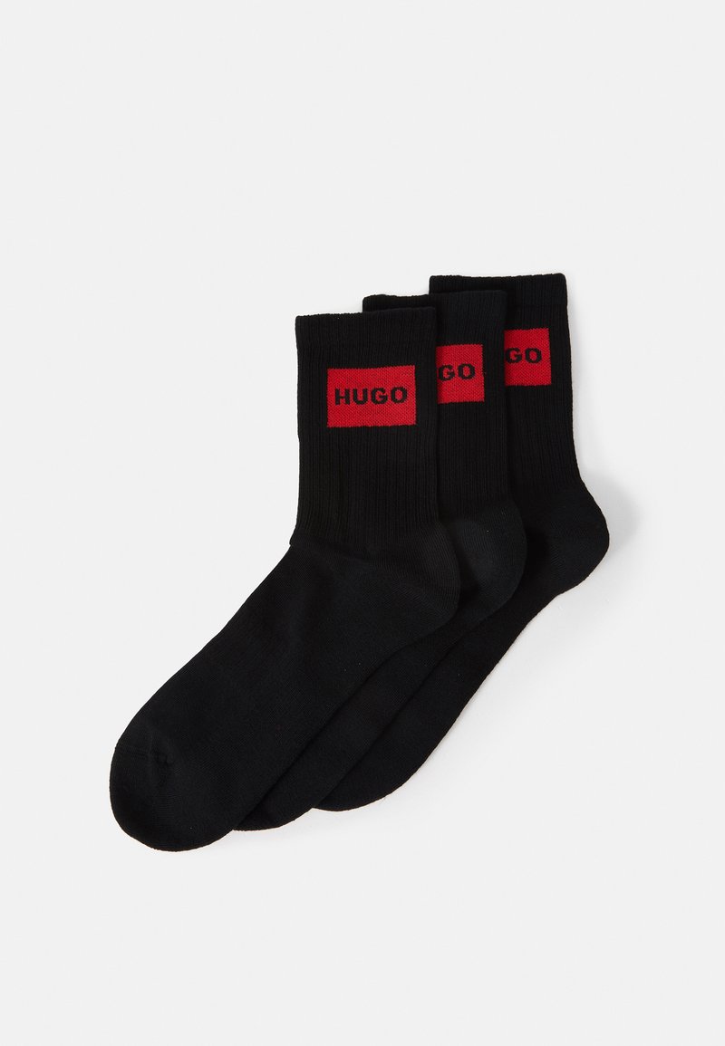 Calcetines de algodón negros con textura acanalada, que presentan acentos rectangulares rojos con el logo "HUGO", presentados en un paquete de tres.