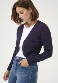 Cardigan navy in tessuto morbido con vestibilità rilassata, apertura frontale e maniche lunghe, abbinato a jeans a vita alta di colore blu chiaro.