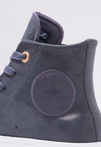 Gros plan sur une sneaker Converse All Star montante grise montrant le logo étoile embossé et les lacets avec œillets métalliques.