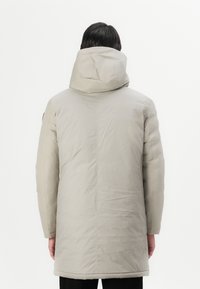 Lys beige vandtæt parka med hætte, der har en glat tekstur og en lige pasform, som strækker sig til midtlåret.