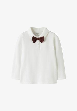 Weißes, langärmeliges Poloshirt aus weichem Stoff, mit einer braunen Fliege am Kragen befestigt. Einfaches und sauberes Design.