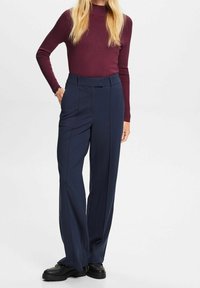 Granatowe spodnie o szerokich nogawkach z wysokim stanem, dopasowanym krojem i szlufkami na pasek, połączone z bordowym prążkowanym topem z długim rękawem. Czarnie buty dopełniają stylizację.