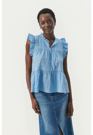 Blouse bleu clair à manches courtes avec des manches volantes, motif texturé, décolleté en V et taille empire, associée à une jupe en denim.