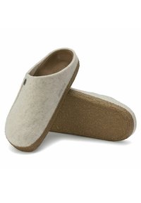 Felt slippers in cream color with a rounded toe, cork sole, and subtle stitching detail. One slipper is partially visible.