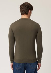 Maglione verde oliva a maniche lunghe con collo a girocollo e polsini a coste. Realizzato in un morbido tessuto lavorato a maglia, presenta un orlo dritto e un design minimal.