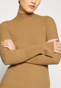 Ribbed turtleneck-sweateri beige-värissä, jossa on pitkät hihat ja tiukka malli, joka takaa mukautuvan istuvuuden. Pehmeä tekstuuri ja korkea kaula-aukko.