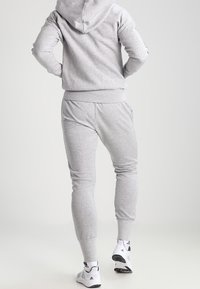 Felpa grigia con cappuccio e pantaloni sportivi abbinati realizzati in tessuto morbido, vestibilità slim con polsini e vita elasticizzati, abbinati a sneakers bianche.