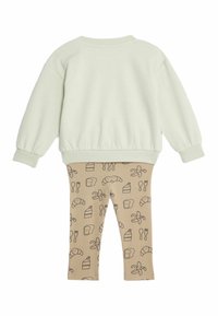Felpa in cotone verde chiaro con spalle cadenti abbinata a leggings beige con motivi a tema alimentare neri: cornetti, torte e posate.
