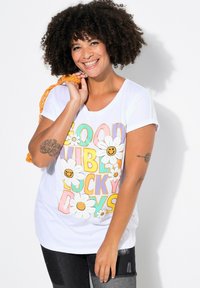 T-shirt blanc à manches courtes avec un texte multicolore disant "Good Vibes Lucky Days", agrémenté de marguerites blanches et de visages souriants.