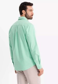 Camicia a maniche lunghe verde chiaro con colletto button-down, piega sul retro e maniche con polsino. Texture liscia e design aderente.