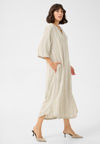 Abito a righe crema e beige con scollatura a V, maniche corte, tasche laterali e silhouette fluida, abbinato a mule beige con tacco.