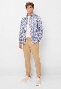 Bloemige shirt in blauwe en beige tinten, lange mouwen, sluiting met knopen aan de voorkant. Gecombineerd met beige broeken en lichtgekleurde sneakers.
