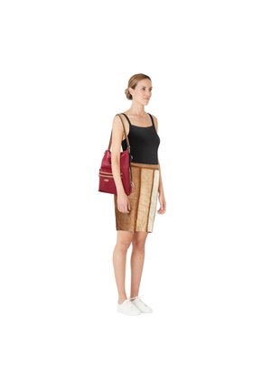 Schwarzes Tanktop, brauner Rock mit cremefarbenen Seitenpanelen, weiße Sneakers, trägt eine rote Tasche mit goldfarbenem Reißverschluss, minimalistisches Design und weiche Textur.