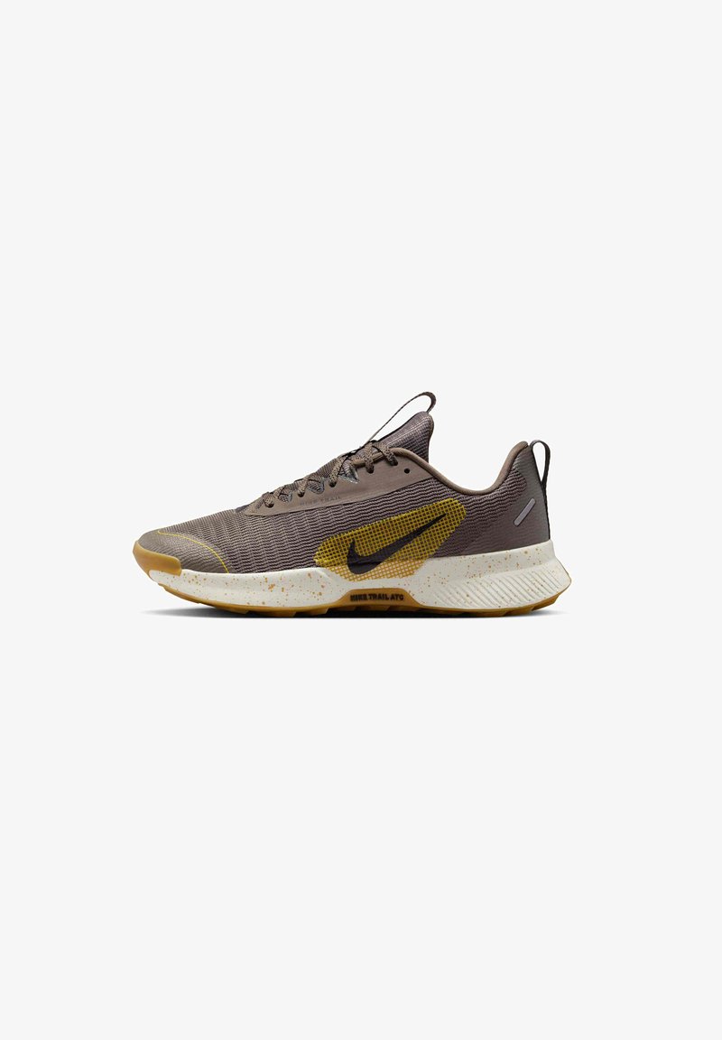 Brown athletic shoe with mesh upper, yellow accents, textured sole, and visible speckles. Lace-up design with a pull tab on the heel.