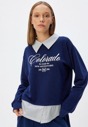 Sudadera azul marino con el texto en blanco "Colorado" y cuello a rayas. Presenta una capa inferior que asoma en el dobladillo, mangas largas y un corte relajado.