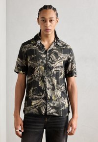 Camicia a maniche corte nera con un motivo astratto giallo e grigio. Presenta un'apertura con bottoni davanti e un colletto con accessori decorativi.