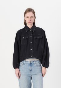 Giacca di jeans nera cropped con colletto a punta, chiusura frontale con bottoni, due tasche sul petto e maniche rilassate su uno sfondo semplice.