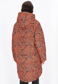 Vadderad jacka med en orange bas och svart samt blå leopardmönster, en huva och en medellång design. Texturerat tyg med kviltat mönster.