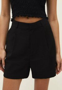 Pantalones cortos ajustados negros hechos de una tela ligera, con un diseño frontal plano, bolsillos laterales y un ajuste relajado, terminando por encima de la rodilla.
