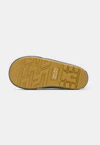 Semelle de chaussure avec semelle jaune, motifs géométriques, et étiquette "Fabriqué en Chine" en texte blanc sur fond jaune.