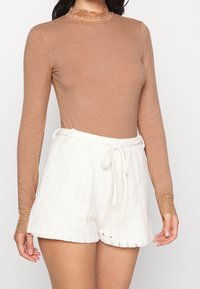 Ribbade långärmade topp i ljusbrun färg med spetsdetaljer, kombinerad med vita, strukturerade shorts med dragsko i midjan och skålad kant.