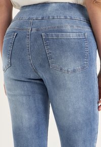 Ljusblå denimjeans med medelhög midja, bakfickor och en slät textur med subtila blekningar.