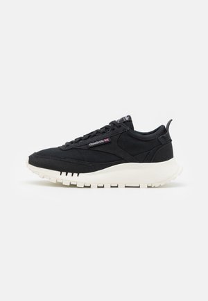 Sorte sneakers lavet af stof med en tekstureret overflade, der har en tyk hvid sål og subtil Reebok-branding på siden.
