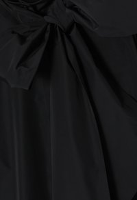 Schwarzes Kleid mit einer Schleifendetail am Ausschnitt. Der Stoff ist glatt und leicht, mit drapierten Schichten und dezentem Glanz.