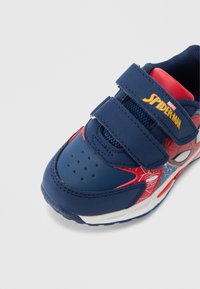 Adidaș albastru și roșu cu design Spiderman, având partea superioară texturată, benzi velcro, găuri de ventilație și talpă de cauciuc durabilă.