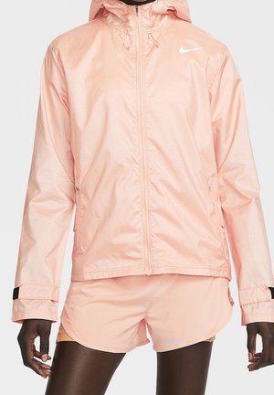 Veste Nike légère de couleur rose pâle, avec fermeture éclair, capuche et poignets élastiques. Présente une texture subtile et un logo réfléchissant.