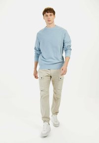 Hellblaues Baumwoll-Sweatshirt mit langen Ärmeln, kombiniert mit beigen Cargo-Hosen mit Seitentaschen und elastischen Bündchen, getragen mit weißen Sneakers.