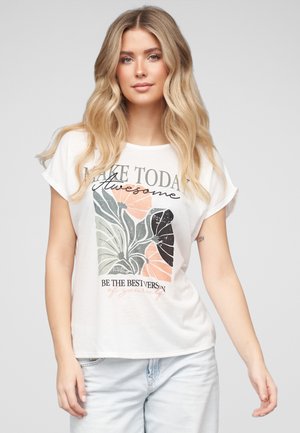 Ung kvinne med langt blondt hår har på seg en hvit t-skjorte med abstrakt bladmotiv og teksten "Make today awesome" samt lyseblå jeans.