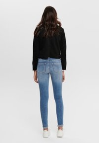 Zwart suède cropped jack over blauwe skinny jeans met lichte vervaging, met twee achterzakken, gecombineerd met witte sneakers.